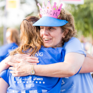 Girls on the Run coach is smiling and wearing a 5k crown while hugging a participant. 